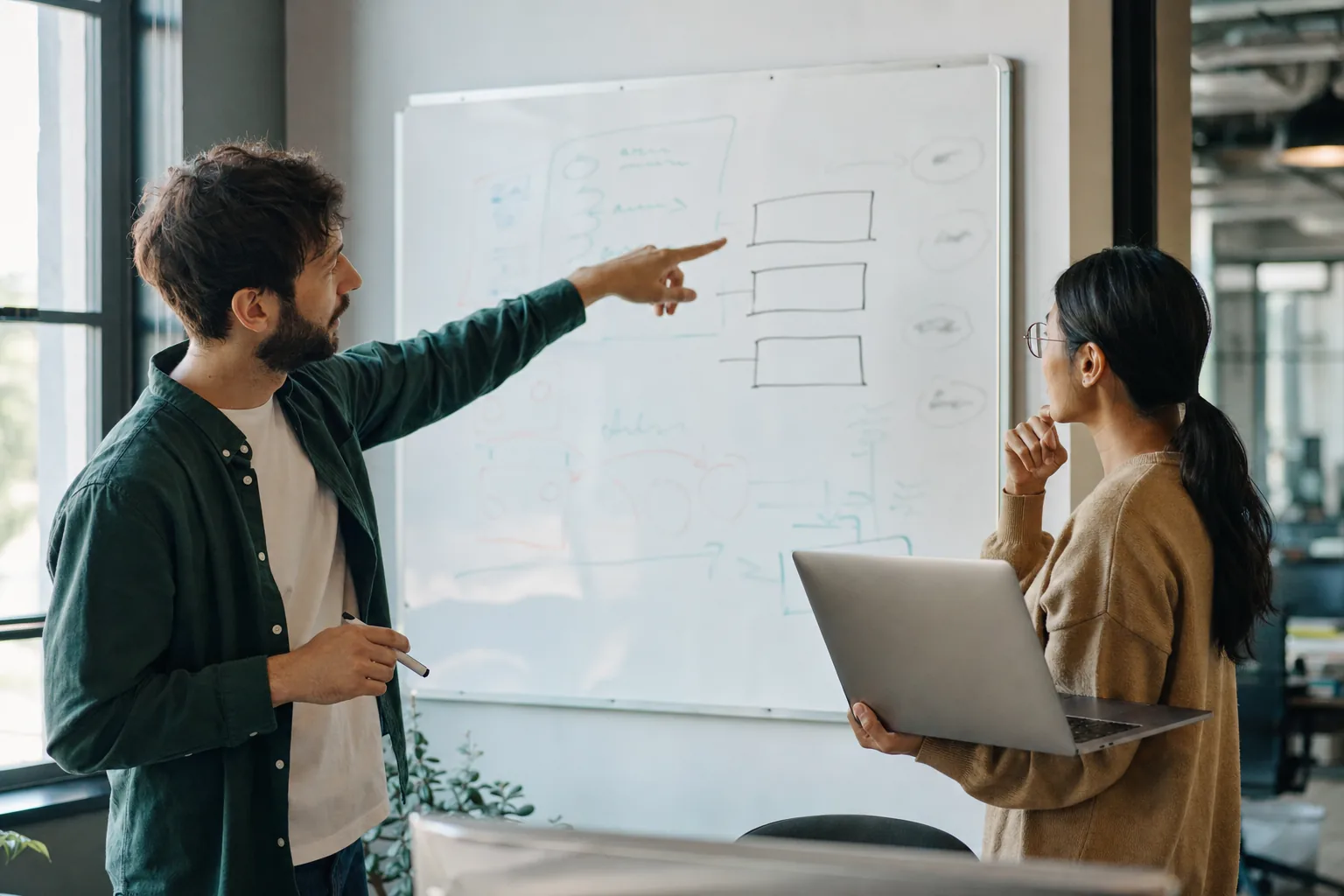 Two people at a whiteboard in an IT office, one pointing at three empty boxes drawn on it, deciding who gets to create agents