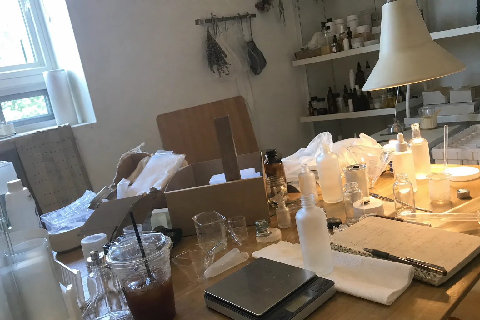 A beauty brand’s workbench: a phone on a tripod filming half-labelled jars, a scale and shipping boxes